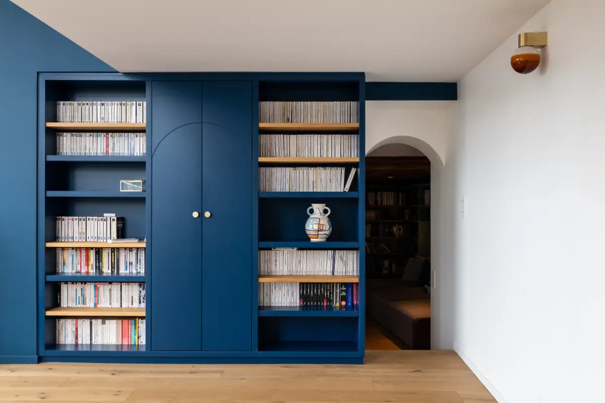 Bibliothèque et placard peints en bleu de la même couleur que le mur. Effet de prolongation