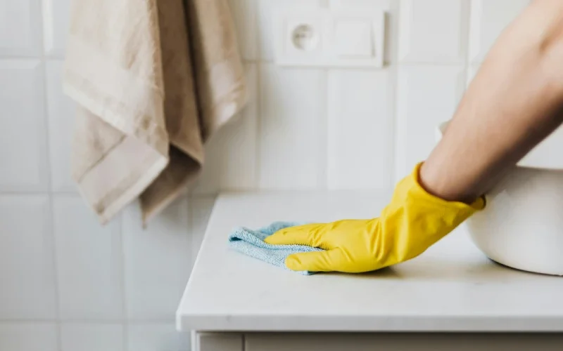 service de ménage à domicile, main avec un gant jaune passant une microfibre sur le meuble d'un évier